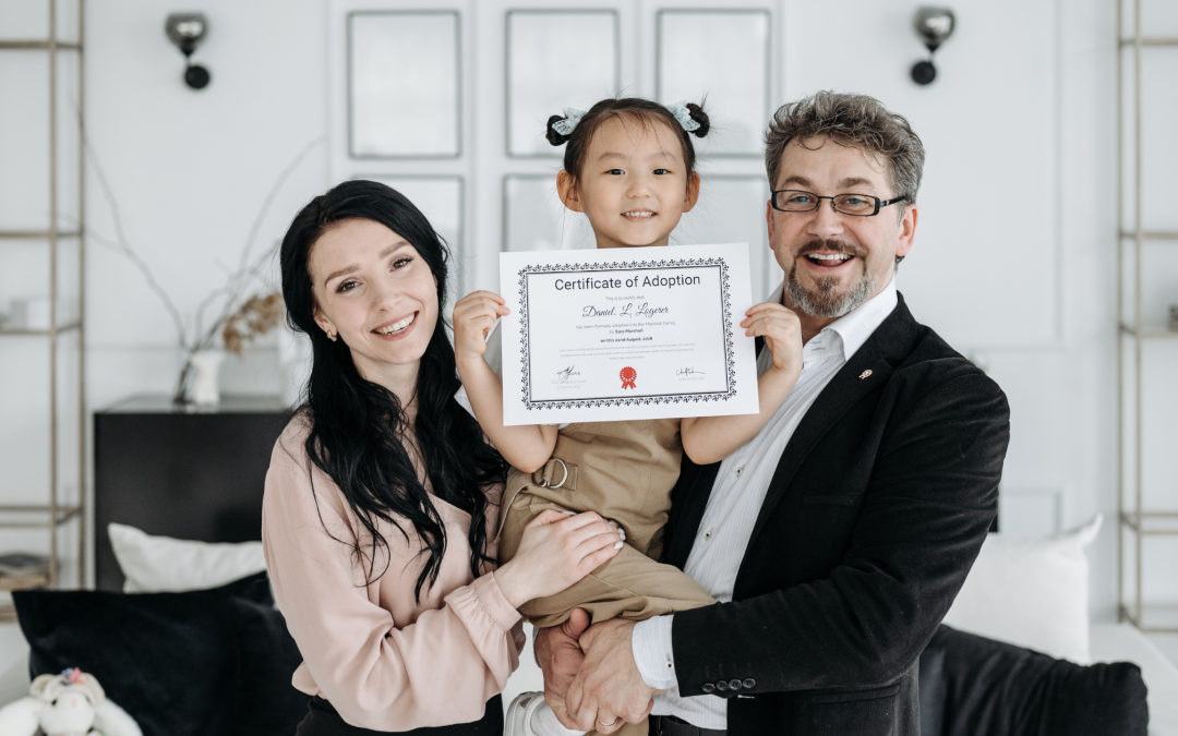 Two parents carrying child holding adoption certificate